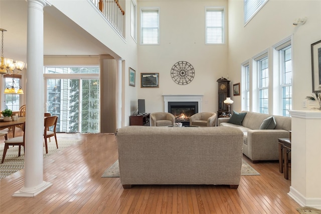 living room featuring an inviting chandelier, light hardwood / wood-style floors, a high ceiling, and ornate columns