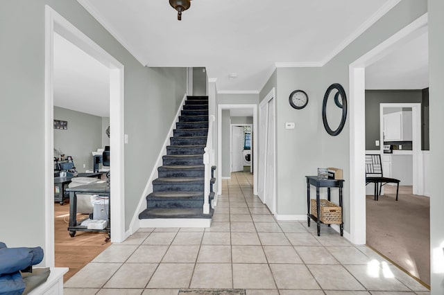 foyer featuring light tile patterned flooring, crown molding, baseboards, and stairs