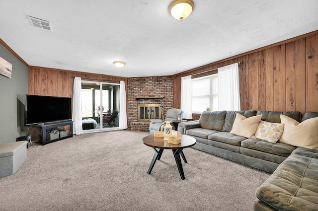 carpeted living area with crown molding, a fireplace, visible vents, wooden walls, and a textured ceiling