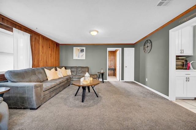 living room featuring wooden walls, visible vents, baseboards, light colored carpet, and ornamental molding