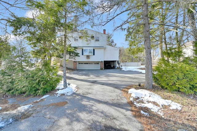 view of property exterior featuring aphalt driveway, brick siding, a chimney, and an attached garage