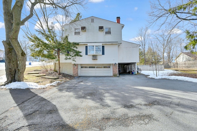 view of property exterior featuring aphalt driveway, a garage, brick siding, fence, and a chimney