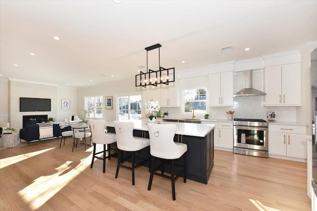 kitchen featuring gas range, a center island, wall chimney range hood, and white cabinets