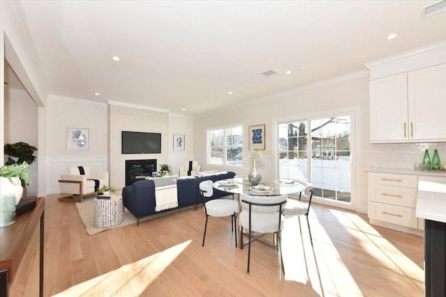 dining area with crown molding, a large fireplace, and light wood-type flooring