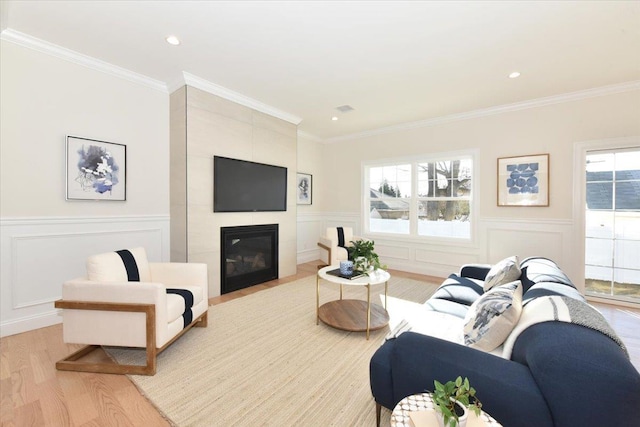 living room with a tiled fireplace, crown molding, and light wood-type flooring