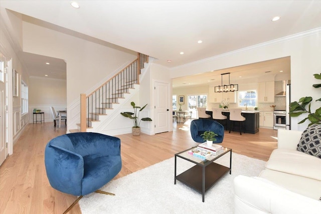 living room with crown molding, an inviting chandelier, and light wood-type flooring