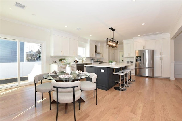 kitchen featuring a kitchen island, high quality fridge, pendant lighting, white cabinetry, and wall chimney range hood