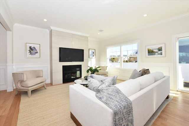 living room featuring crown molding, a healthy amount of sunlight, a large fireplace, and light hardwood / wood-style floors