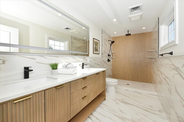 bathroom with a tile shower, tile walls, vanity, and toilet