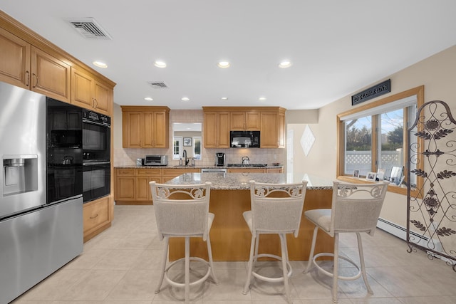 kitchen featuring sink, light stone counters, black appliances, a center island, and backsplash