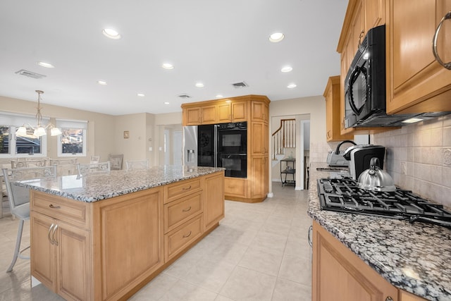 kitchen featuring a kitchen island, pendant lighting, tasteful backsplash, black appliances, and light stone countertops