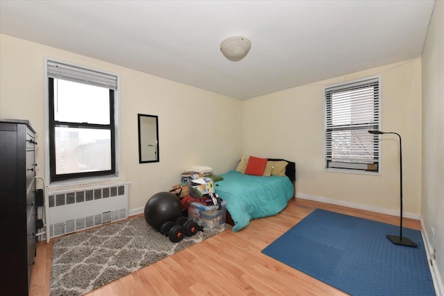 bedroom with radiator heating unit, baseboards, and wood finished floors