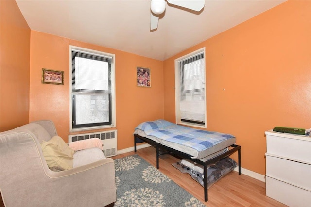 bedroom with radiator, ceiling fan, baseboards, and wood finished floors