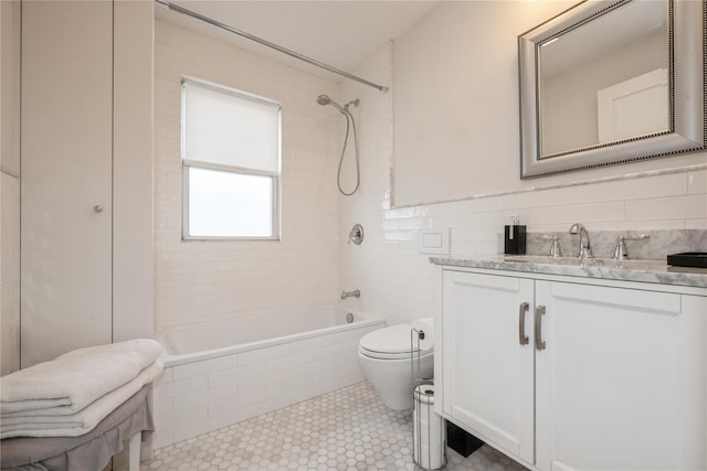 full bathroom featuring tile walls, vanity, tiled shower / bath, and toilet