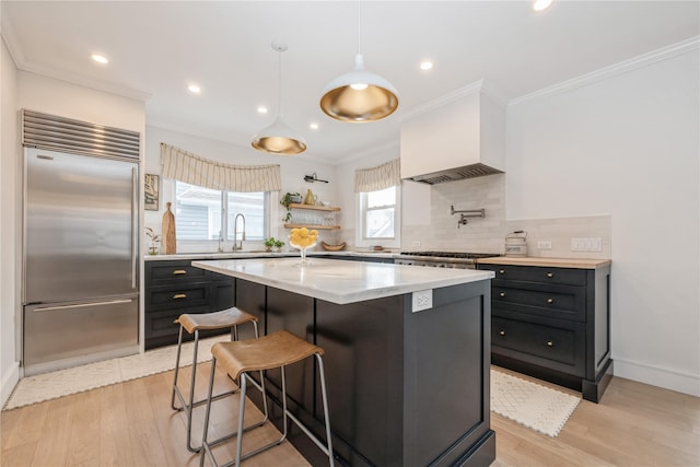 kitchen with a kitchen bar, decorative light fixtures, built in fridge, a kitchen island, and custom range hood