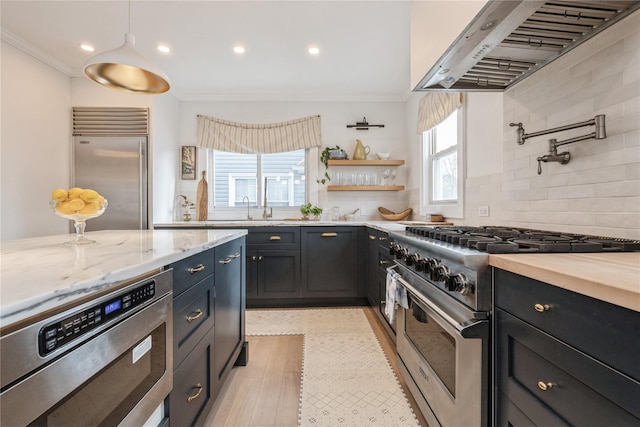 kitchen with premium appliances, decorative backsplash, light stone counters, crown molding, and wall chimney range hood