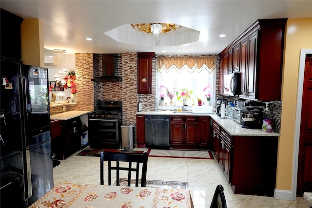 kitchen featuring a tray ceiling, sink, decorative backsplash, black appliances, and wall chimney exhaust hood