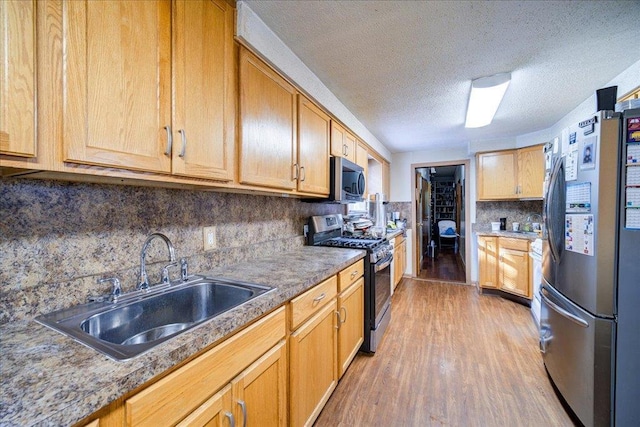 kitchen featuring sink, tasteful backsplash, wood-type flooring, a textured ceiling, and appliances with stainless steel finishes