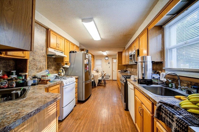 kitchen with sink, a textured ceiling, light wood-type flooring, appliances with stainless steel finishes, and backsplash