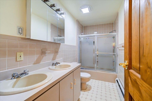 full bathroom with toilet, combined bath / shower with glass door, tile walls, a baseboard radiator, and vanity