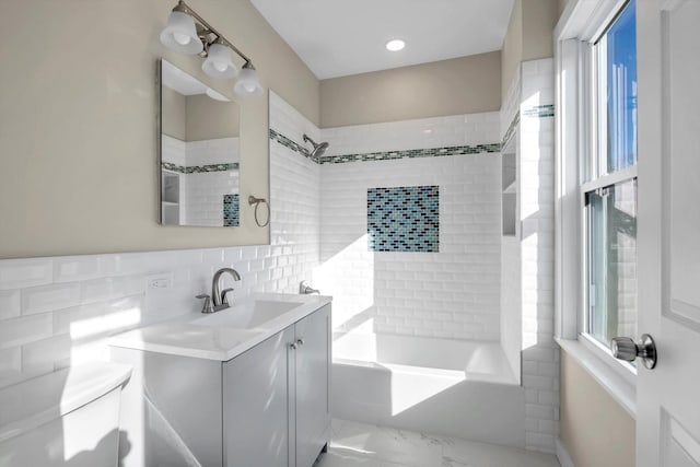 bathroom featuring tiled shower / bath combo, vanity, and tile walls