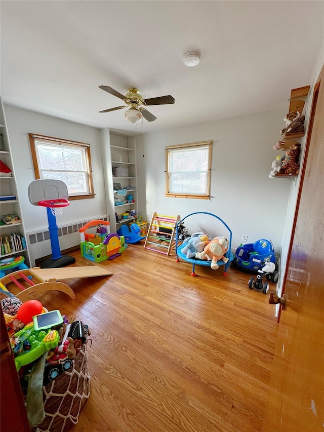 recreation room with ceiling fan, radiator, and hardwood / wood-style floors