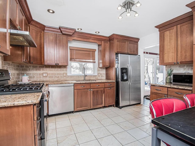 kitchen with sink, decorative backsplash, stainless steel appliances, and light stone countertops