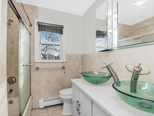 full bathroom featuring toilet, shower / bath combination with glass door, tile walls, vanity, and a baseboard heating unit