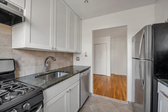 kitchen with appliances with stainless steel finishes, white cabinetry, sink, dark stone countertops, and decorative backsplash