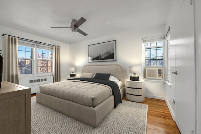 bedroom with multiple windows, ceiling fan, radiator heating unit, and light hardwood / wood-style floors