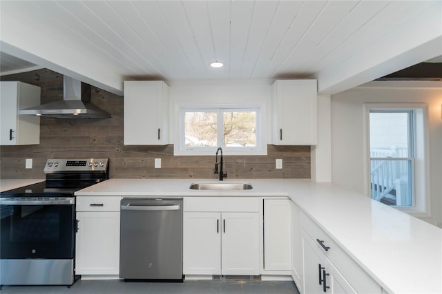 kitchen featuring wall chimney range hood, sink, white cabinets, and appliances with stainless steel finishes