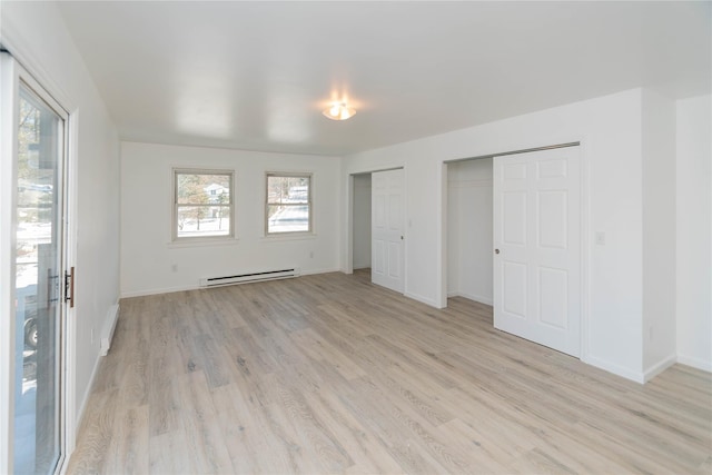 unfurnished bedroom with multiple closets, baseboard heating, and light hardwood / wood-style floors