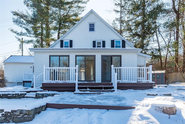 snow covered back of property featuring a shed and a wooden deck