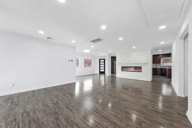 unfurnished living room with a stone fireplace and dark wood-type flooring