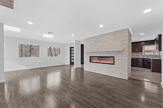 unfurnished living room with a stone fireplace, dark wood-type flooring, and sink