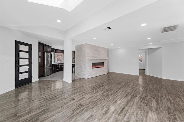 unfurnished living room featuring dark hardwood / wood-style floors, a large fireplace, and vaulted ceiling with skylight