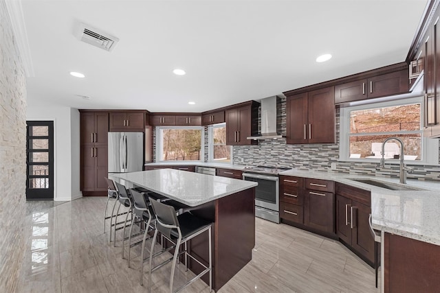 kitchen featuring sink, stainless steel appliances, wall chimney exhaust hood, and light stone countertops