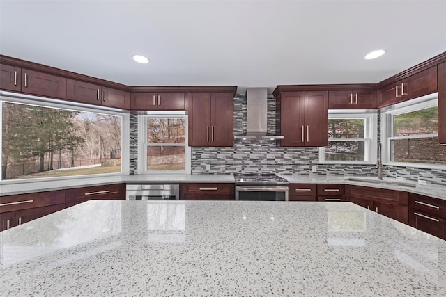 kitchen featuring wall chimney range hood, stainless steel stove, sink, backsplash, and light stone countertops