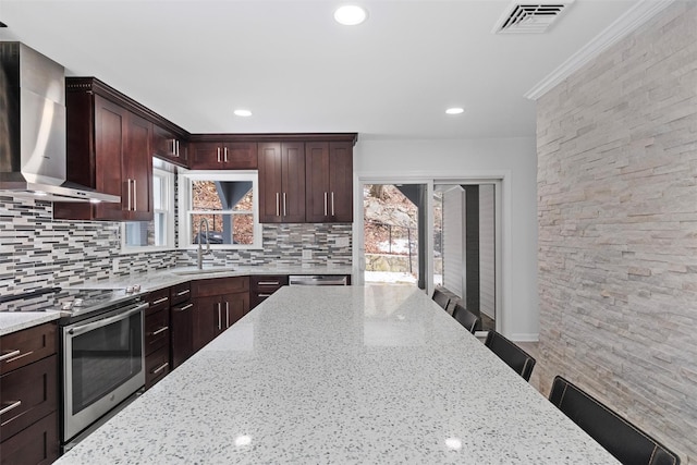 kitchen featuring light stone counters, wall chimney exhaust hood, stainless steel electric stove, and sink