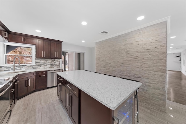 kitchen featuring sink, backsplash, stainless steel appliances, light stone countertops, and a kitchen island