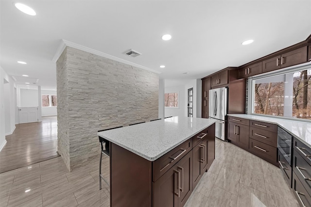 kitchen featuring stainless steel refrigerator, a center island, ornamental molding, light stone countertops, and a kitchen bar