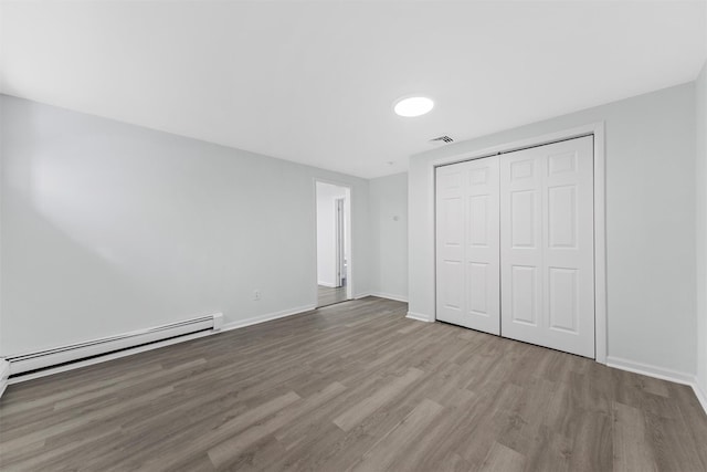 unfurnished bedroom with a baseboard heating unit, a closet, and light wood-type flooring