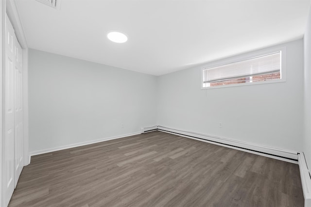 unfurnished room featuring baseboard heating and dark wood-type flooring