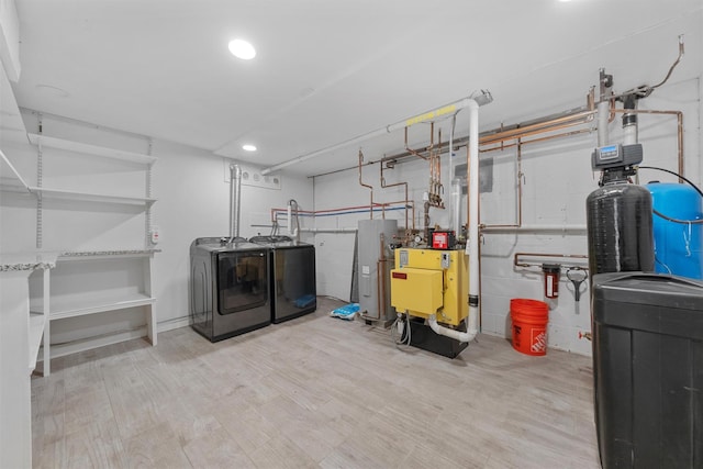 laundry area with electric water heater, washer and clothes dryer, and light hardwood / wood-style floors