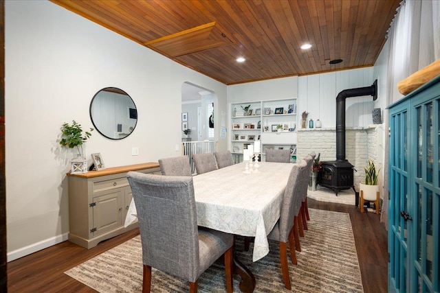 dining room with crown molding, dark wood-type flooring, a wood stove, and wood ceiling