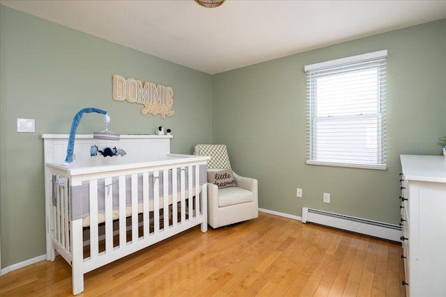 bedroom with a baseboard heating unit, wood-type flooring, and a crib