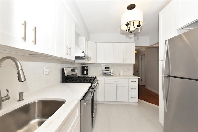 kitchen with stainless steel appliances, light stone countertops, sink, and white cabinets