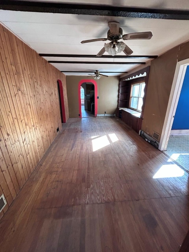 empty room featuring beamed ceiling, ceiling fan, wooden walls, and hardwood / wood-style floors