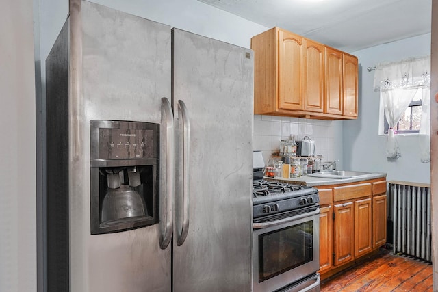 kitchen featuring sink, radiator heating unit, dark hardwood / wood-style flooring, stainless steel appliances, and decorative backsplash