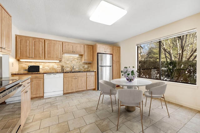 kitchen featuring sink, backsplash, stainless steel appliances, dark stone counters, and light brown cabinets